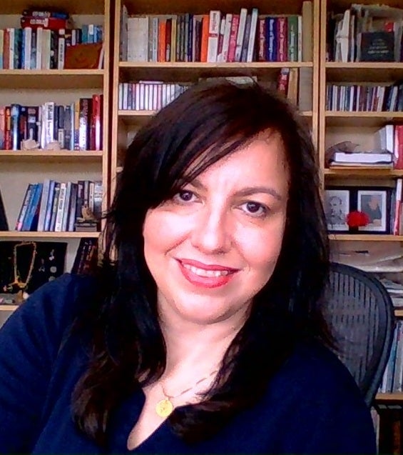 Woman with black hair and a dark blue shirt, smiling in front of bookshelf