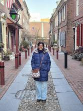Woman outside in long blue coat, smiling, on a sunny day